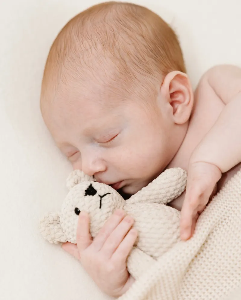 Recém-nascido a dormir, abraçado a um peluche de malha.